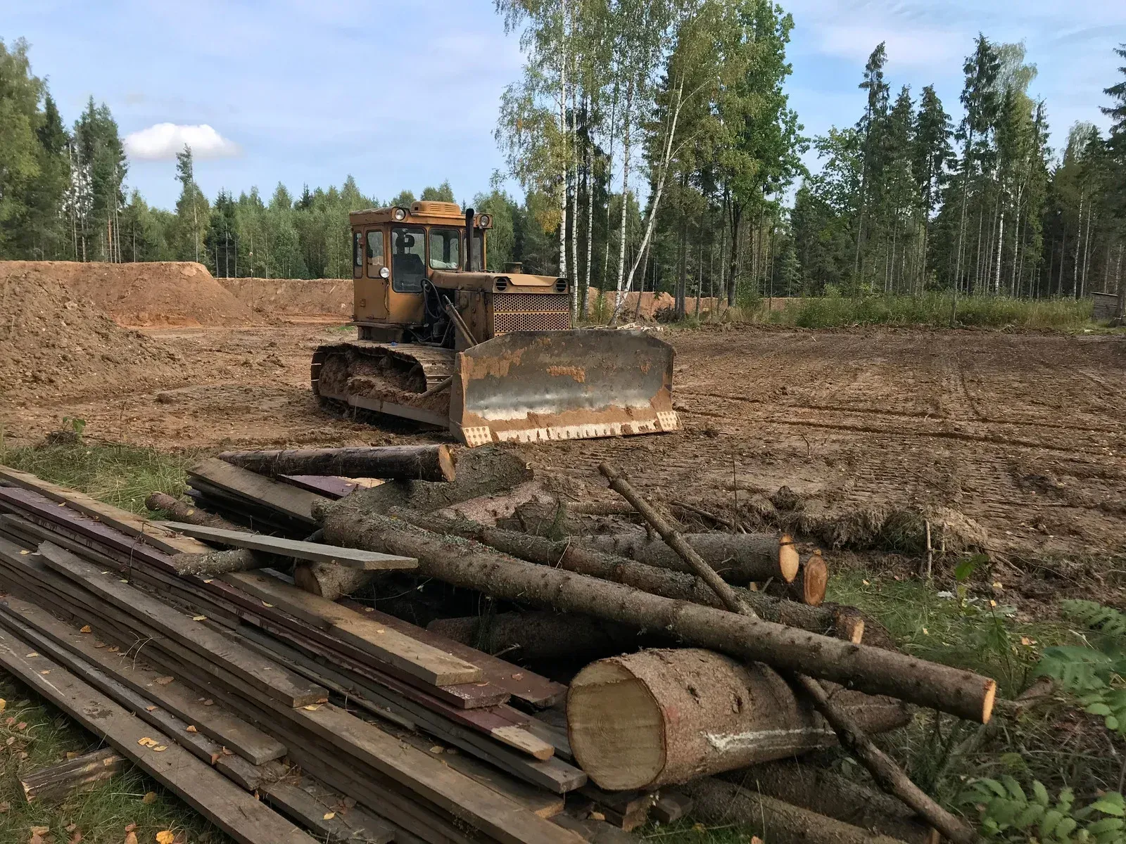 A bulldozer clearing land in a wooded area with logs and lumber in the foreground.