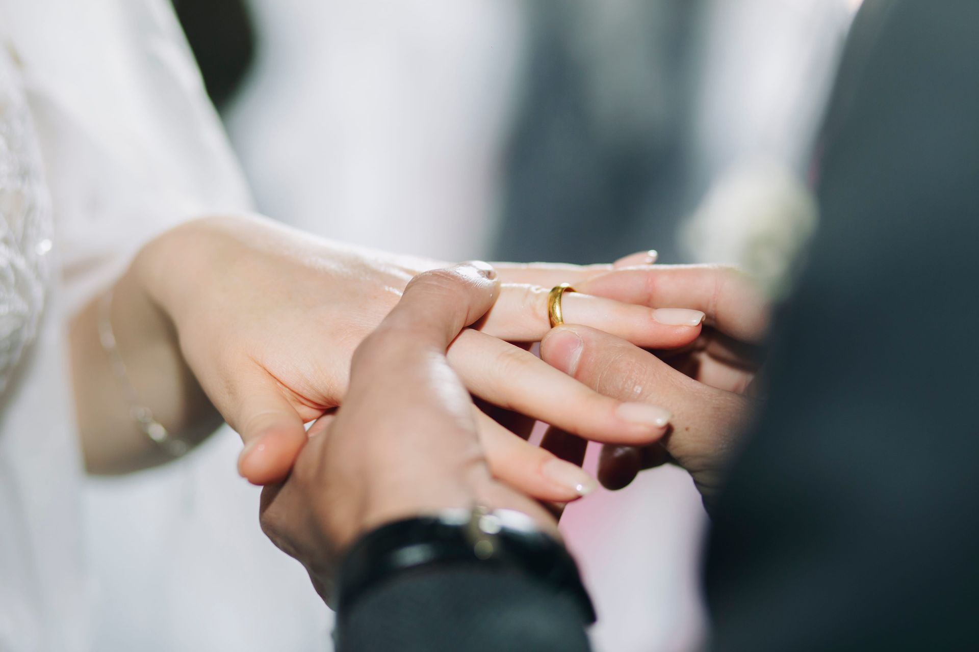 A person gently placing a gold wedding band onto the finger of another person's hand during a wedding ceremony.