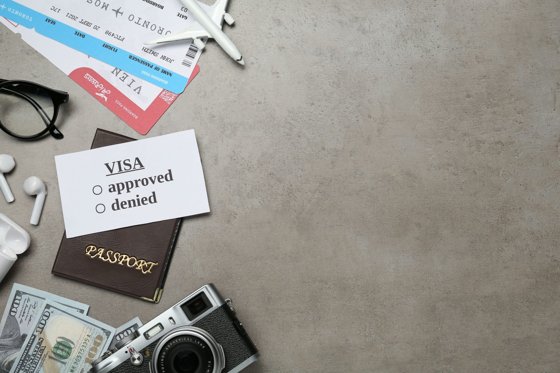 Travel flat lay with passport, boarding pass, camera, sunglasses, earbuds, and a note saying “visa approved, denied”