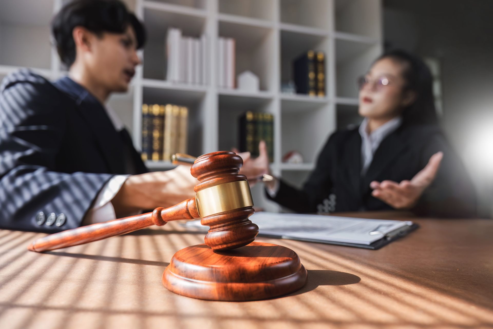 Lawyer’s gavel in foreground with two people discussing a case in an office