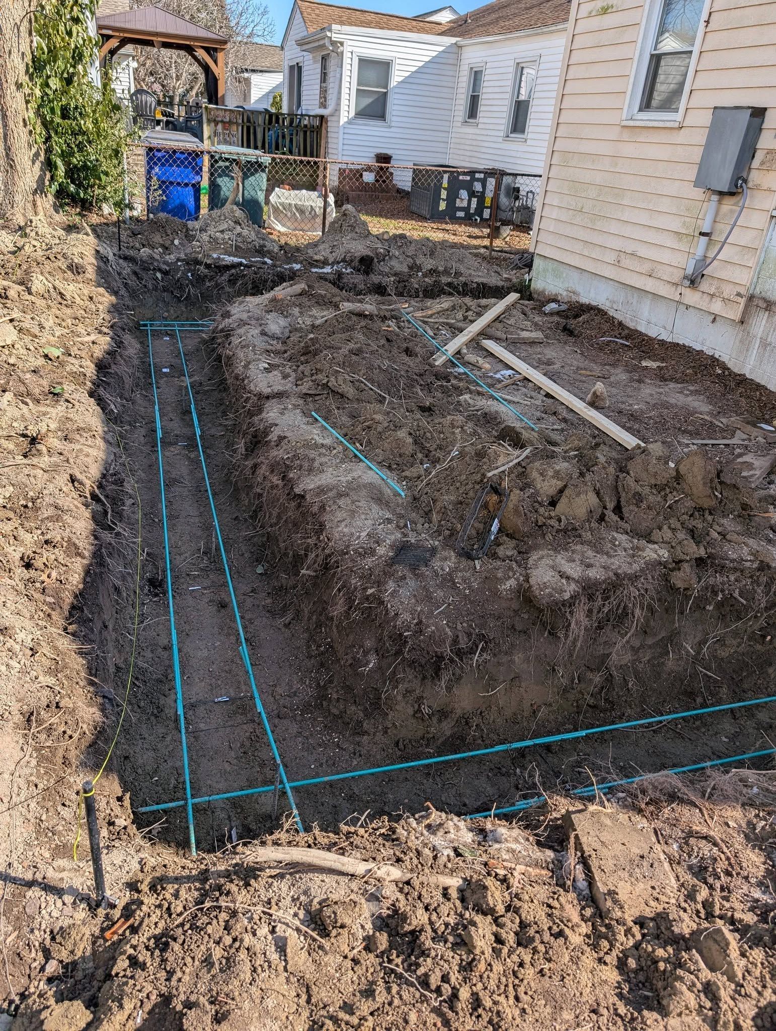 Backyard excavation with dug trench and blue guide lines beside a house and fence