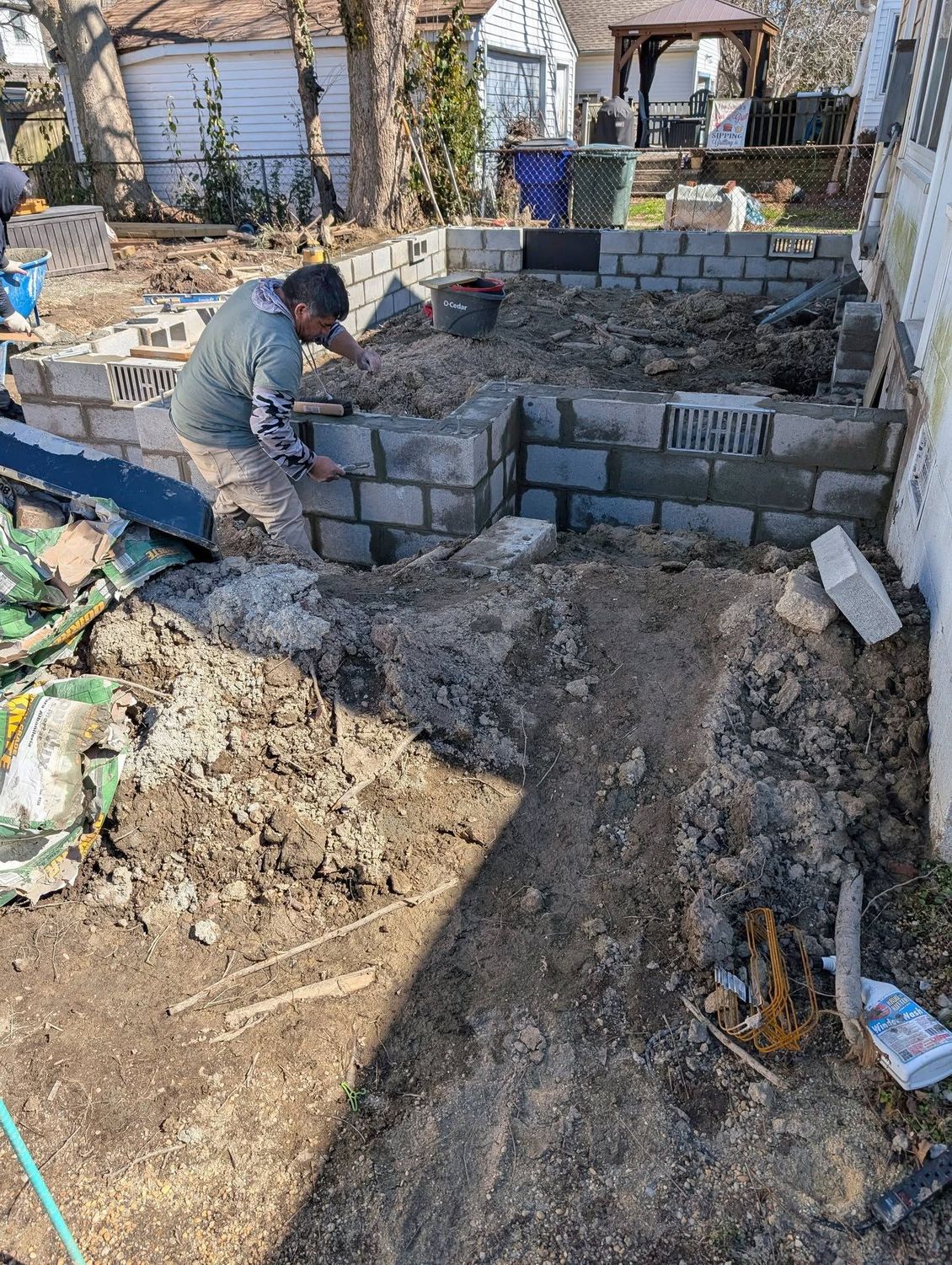 Worker building a stone retaining wall in a dirt-filled backyard garden area