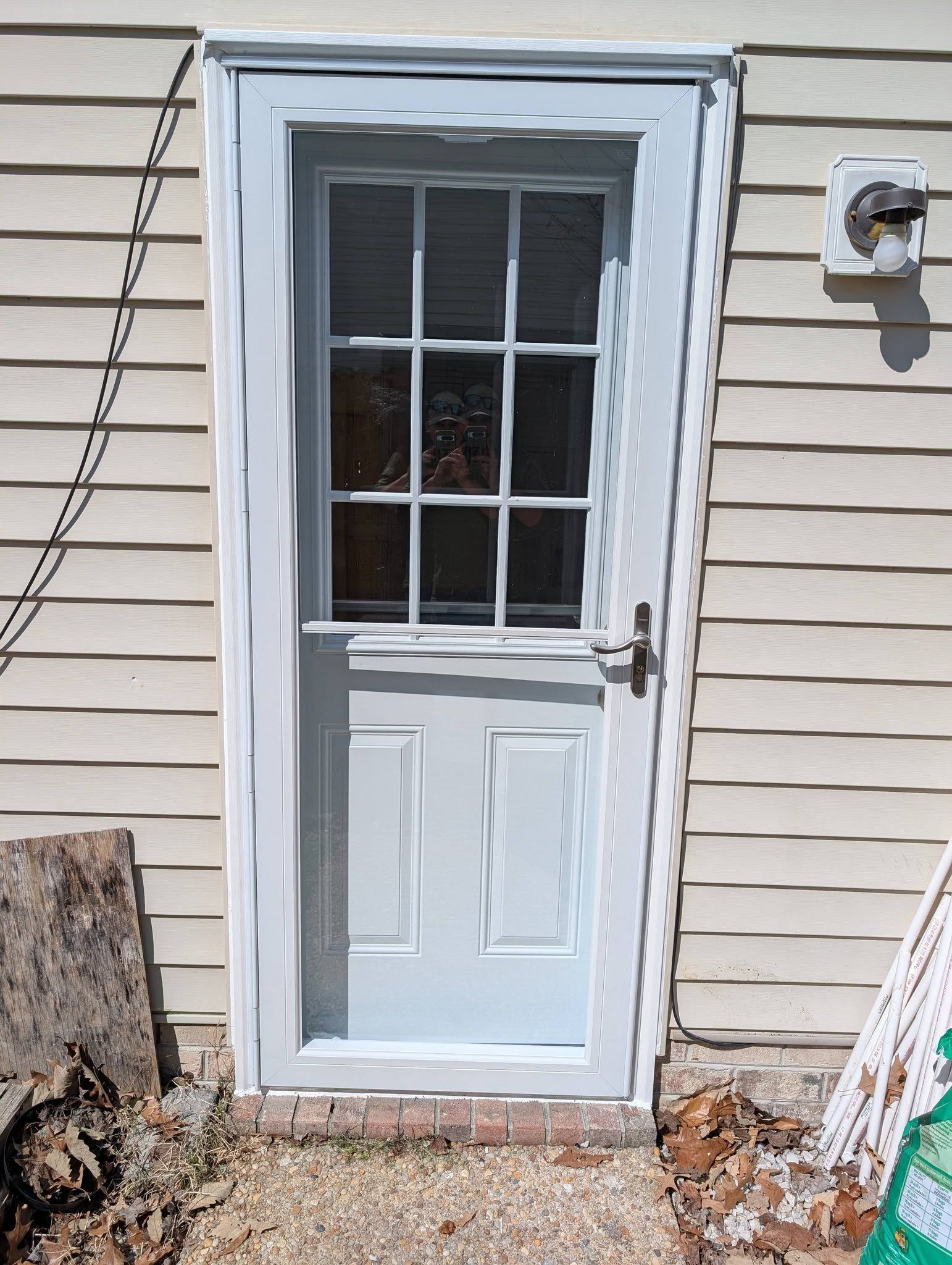 White exterior door with a small window and side latch on beige siding.