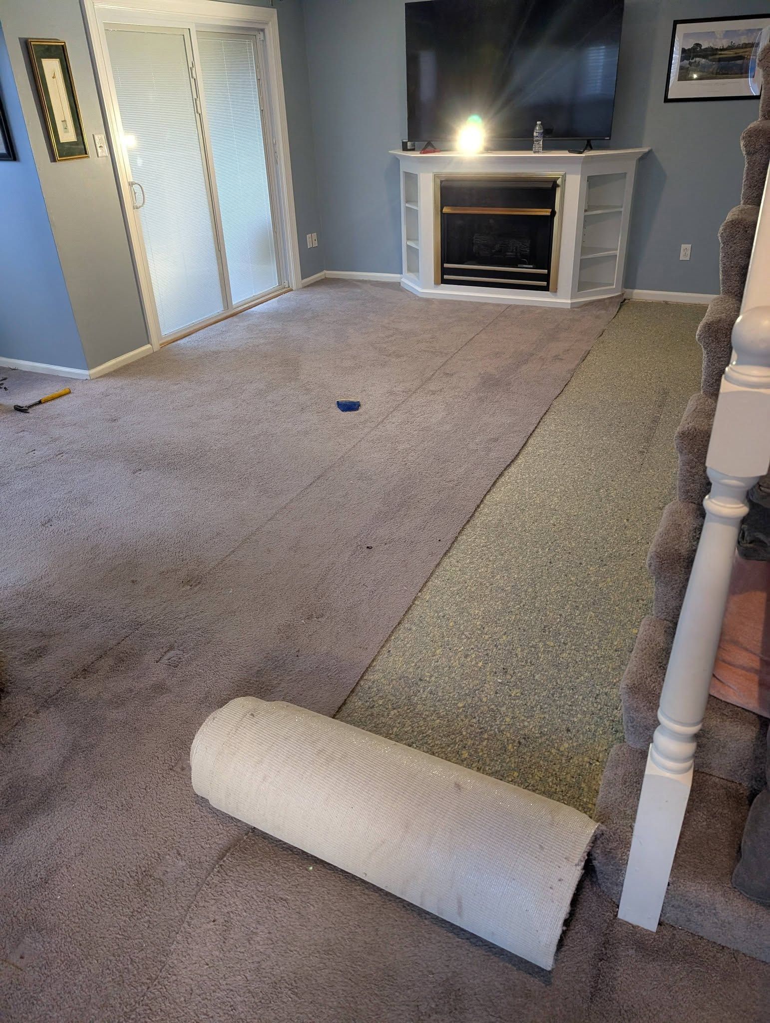 Carpet being installed in a living room with a fireplace and TV.
