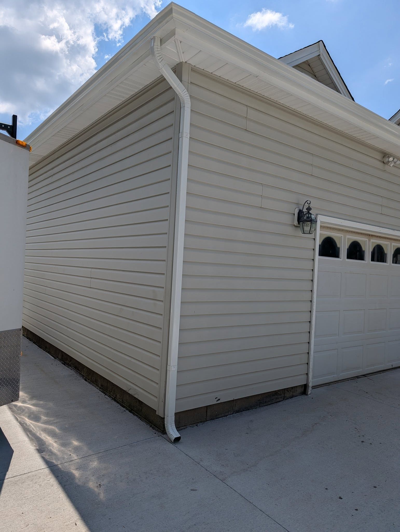 Side view of a beige garage with white trim and a downspout on a snowy driveway