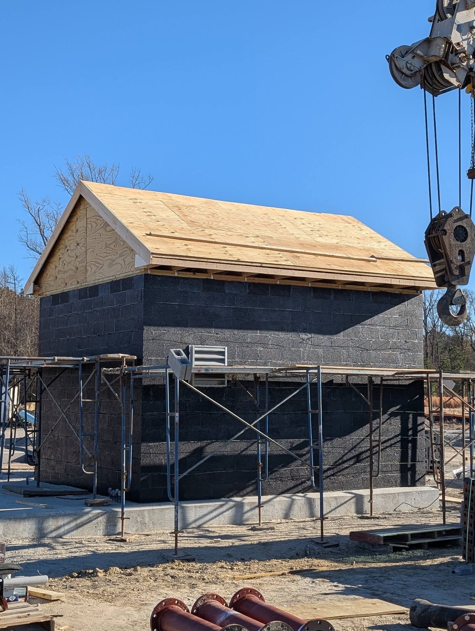 Stone building under construction with wood roof framing and scaffolding against a blue sky