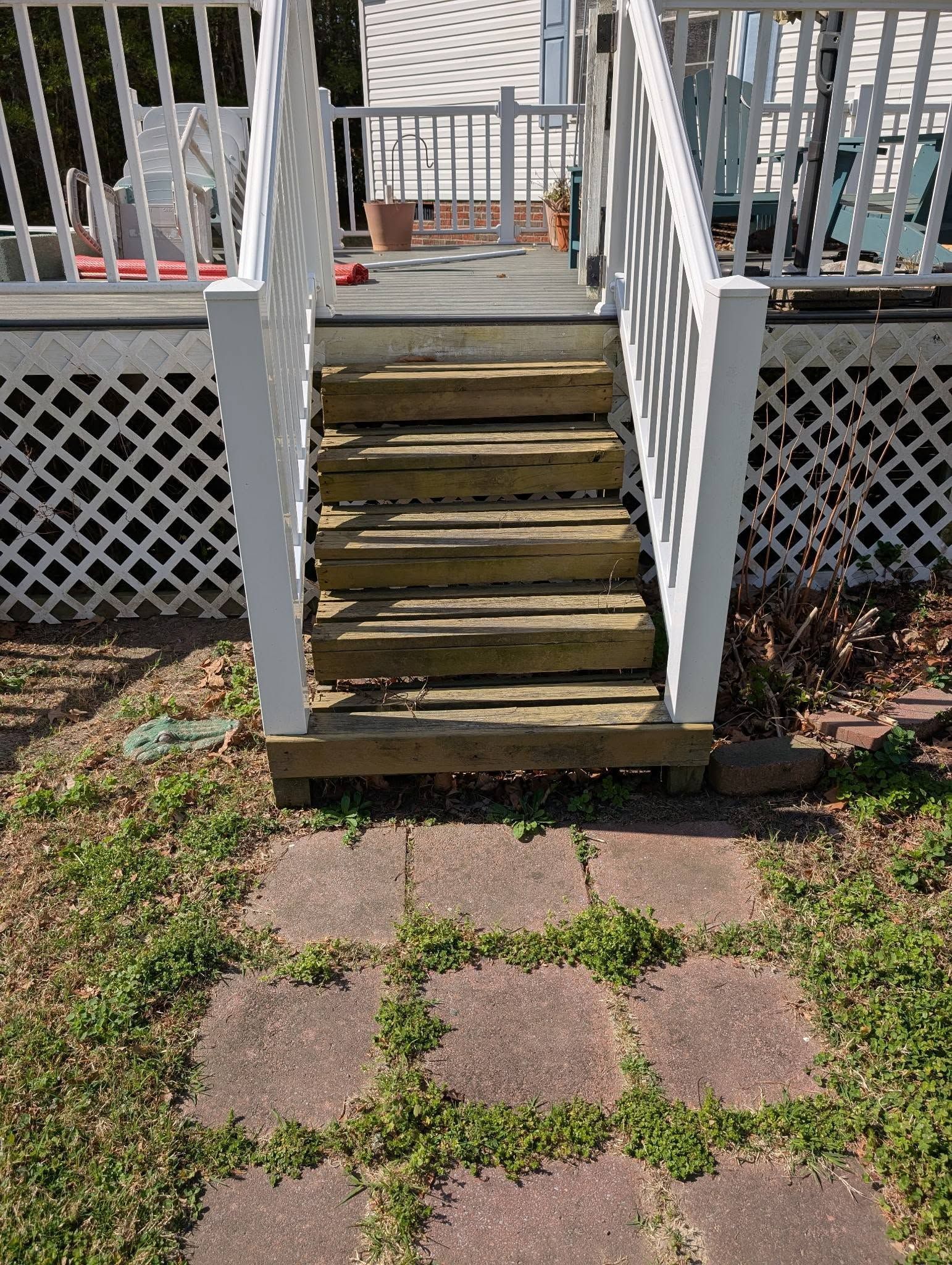 Weathered wooden steps leading up to a white-railed porch over a brick and grass path
