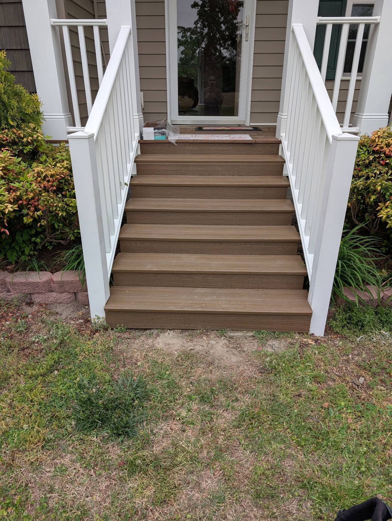 Front steps with white railings leading to a house entrance over a patchy lawn.