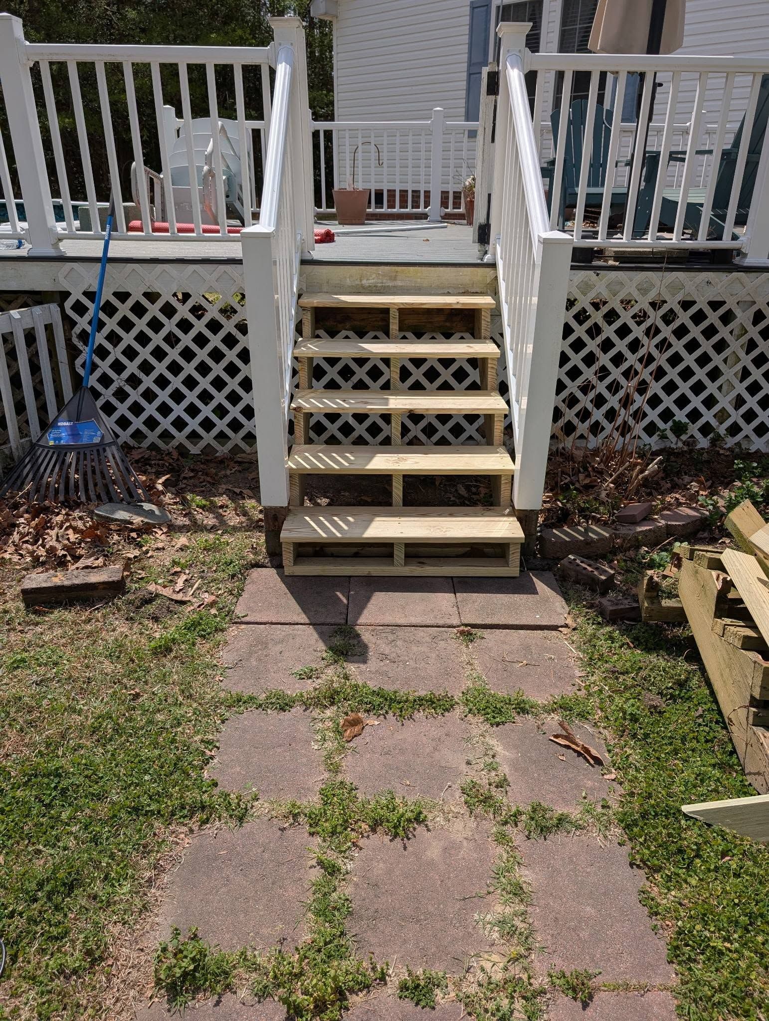 White backyard deck stairs with lattice railing above a stone patio path and grass.