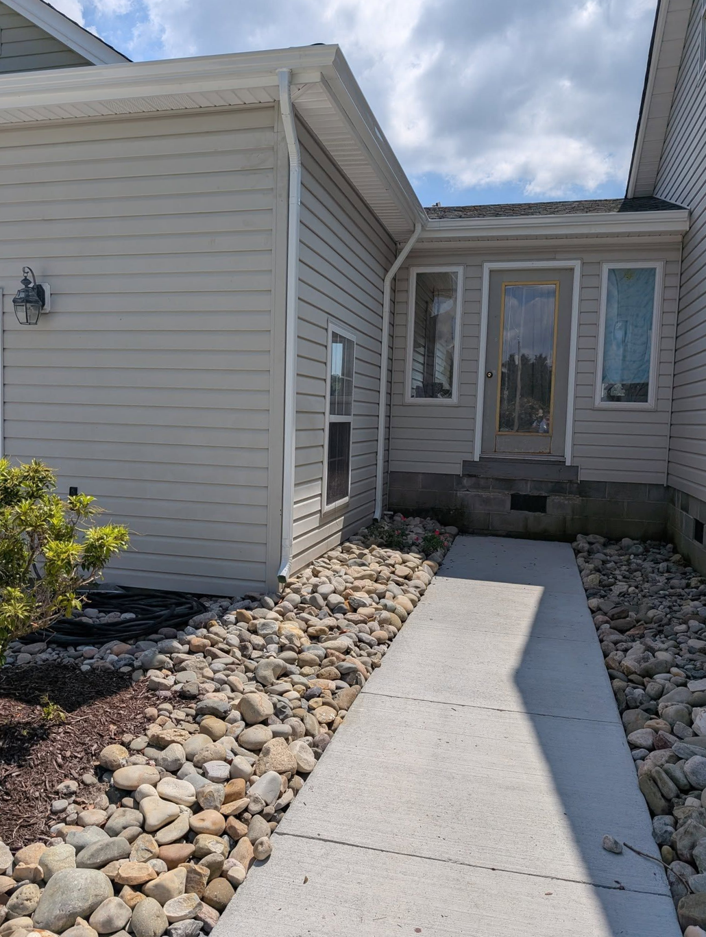 Front walkway leading to a house entrance with white siding and stone landscaping under a cloudy sky