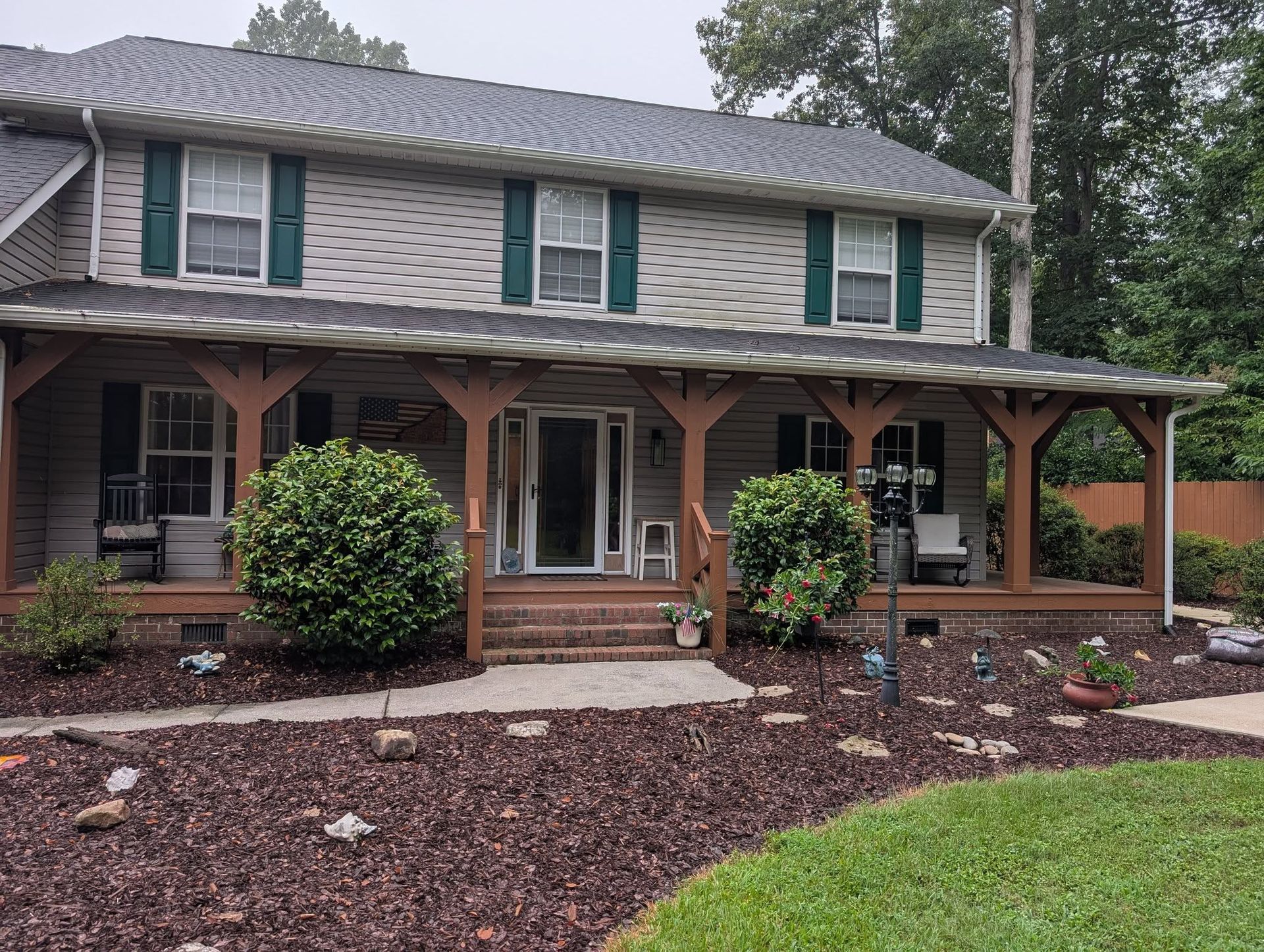 Two-story house with covered front porch, green shutters, and landscaped yard