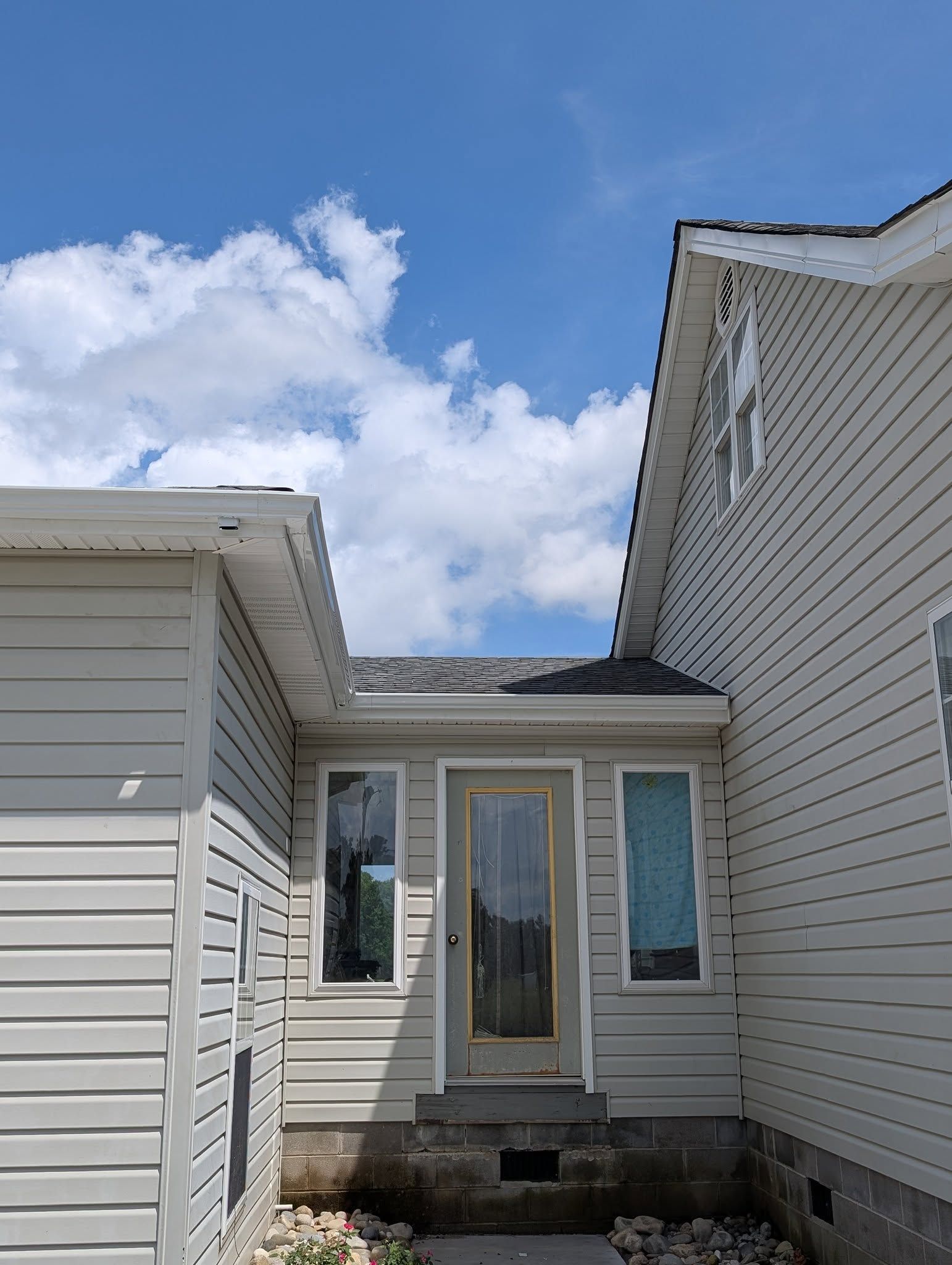 Narrow backyard entryway between two beige houses, with a glass door under a blue sky and clouds.