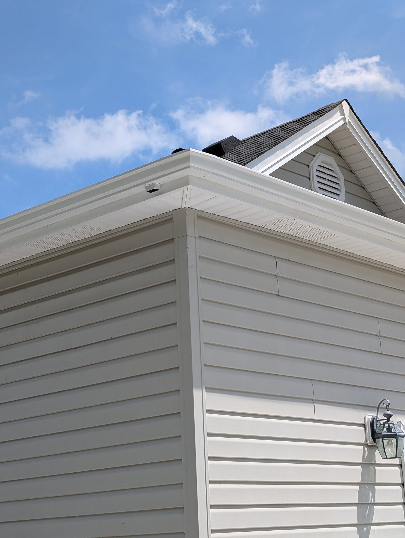 White vinyl-sided house corner with roofline and blue sky above