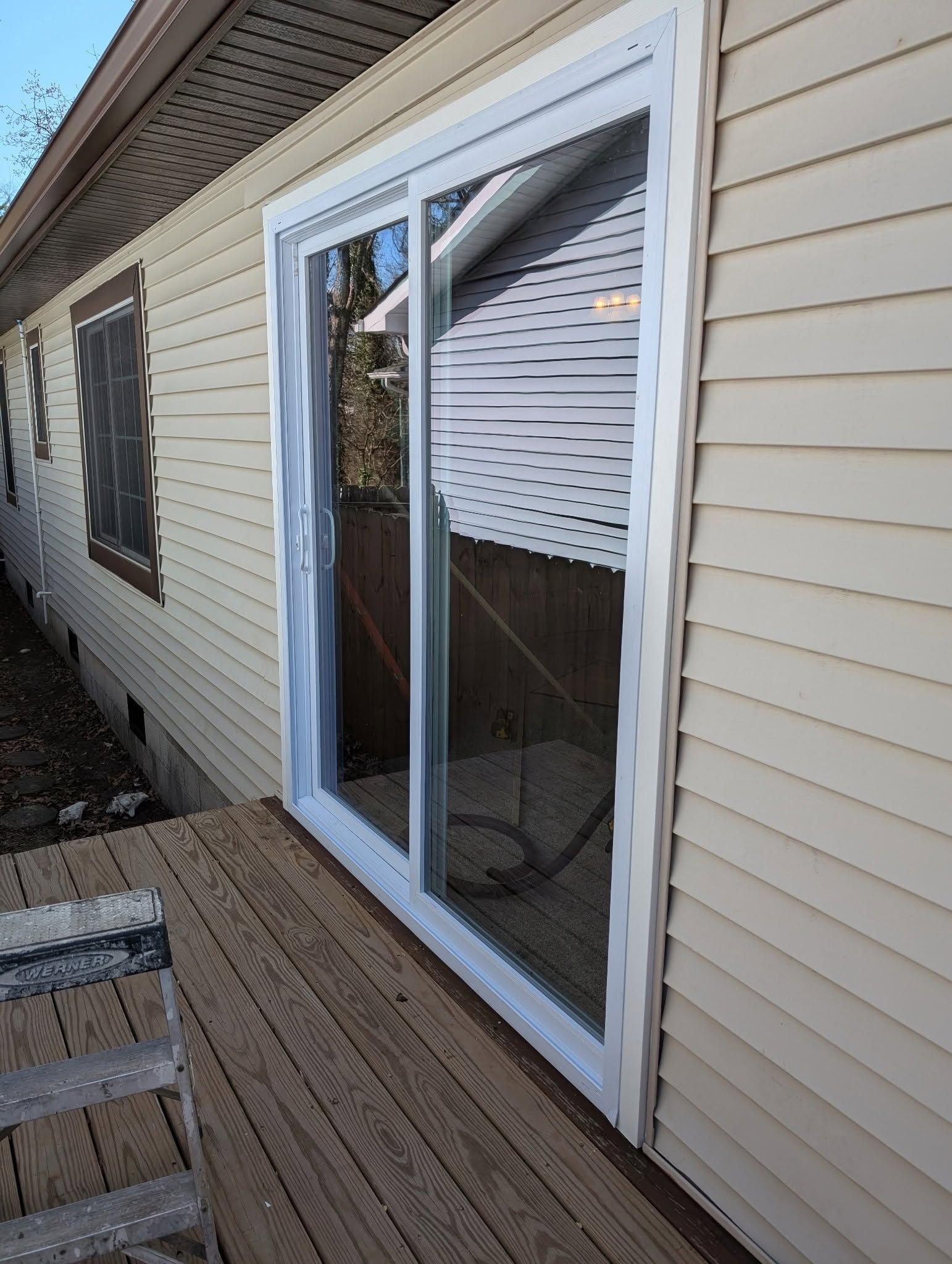 Sliding glass door on a beige house exterior with a deck in the foreground and siding around it