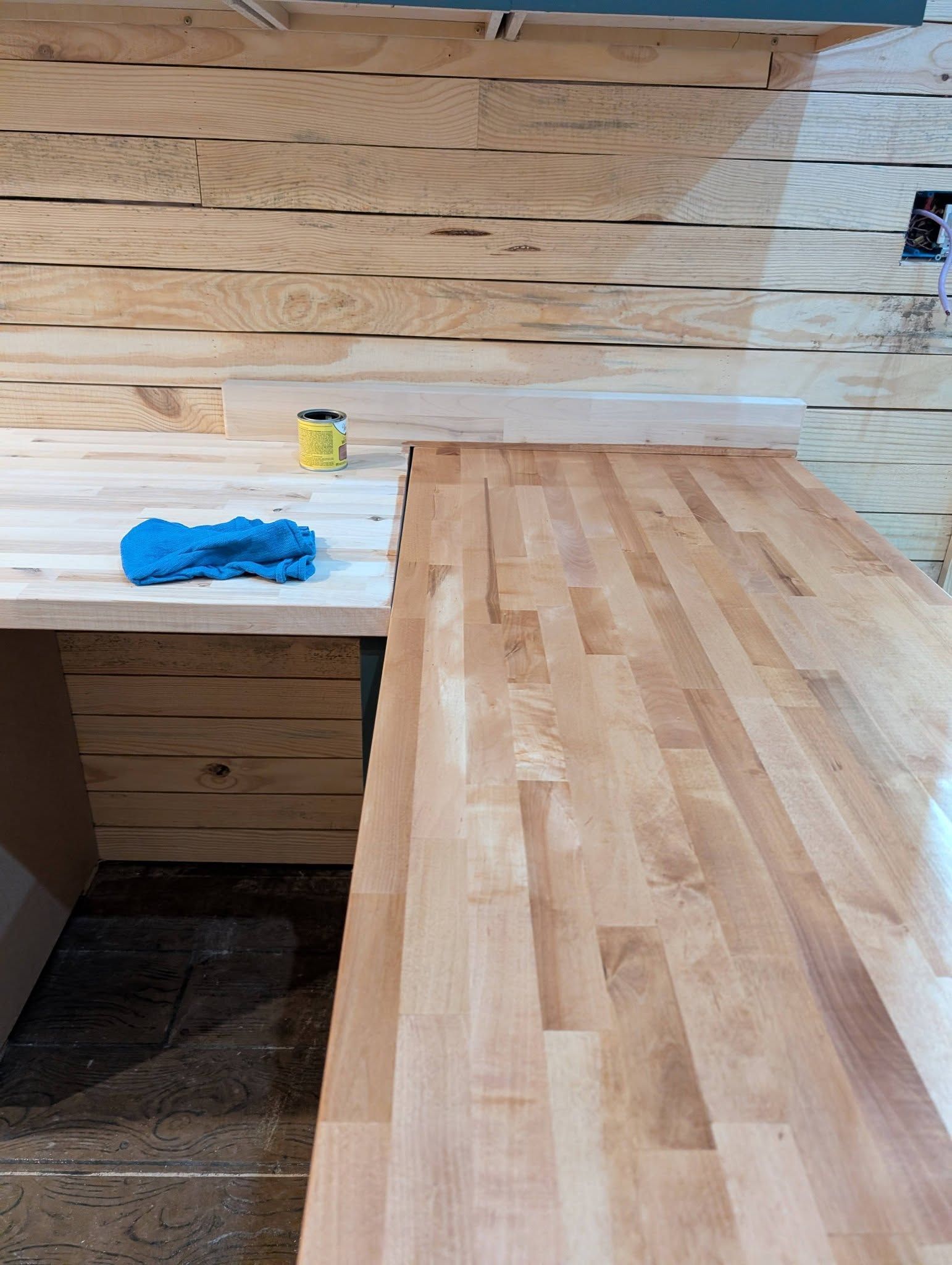 Wooden kitchen countertop and backsplash under construction, with a blue cloth and yellow bottle on the left.