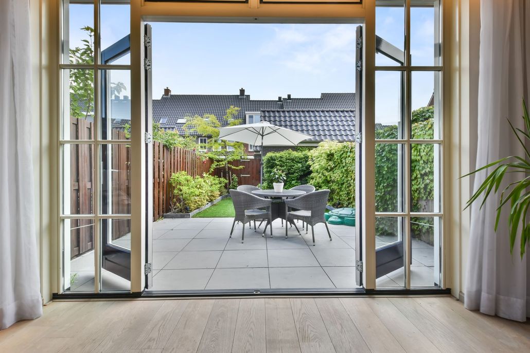 Open patio doors to a sunny backyard with a table and chairs