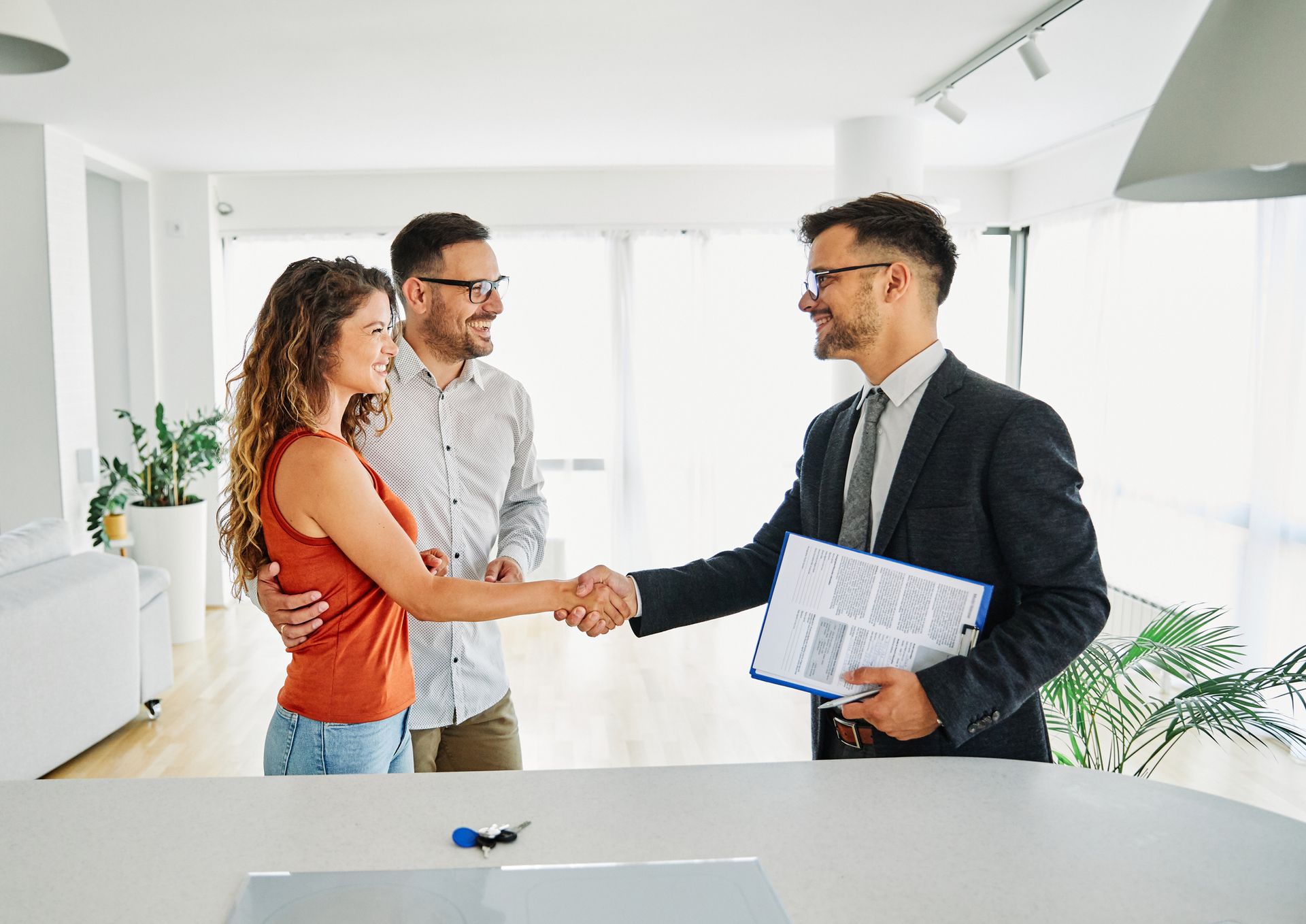Couple shaking hands with a real estate agent inside a modern home; agreement reached.