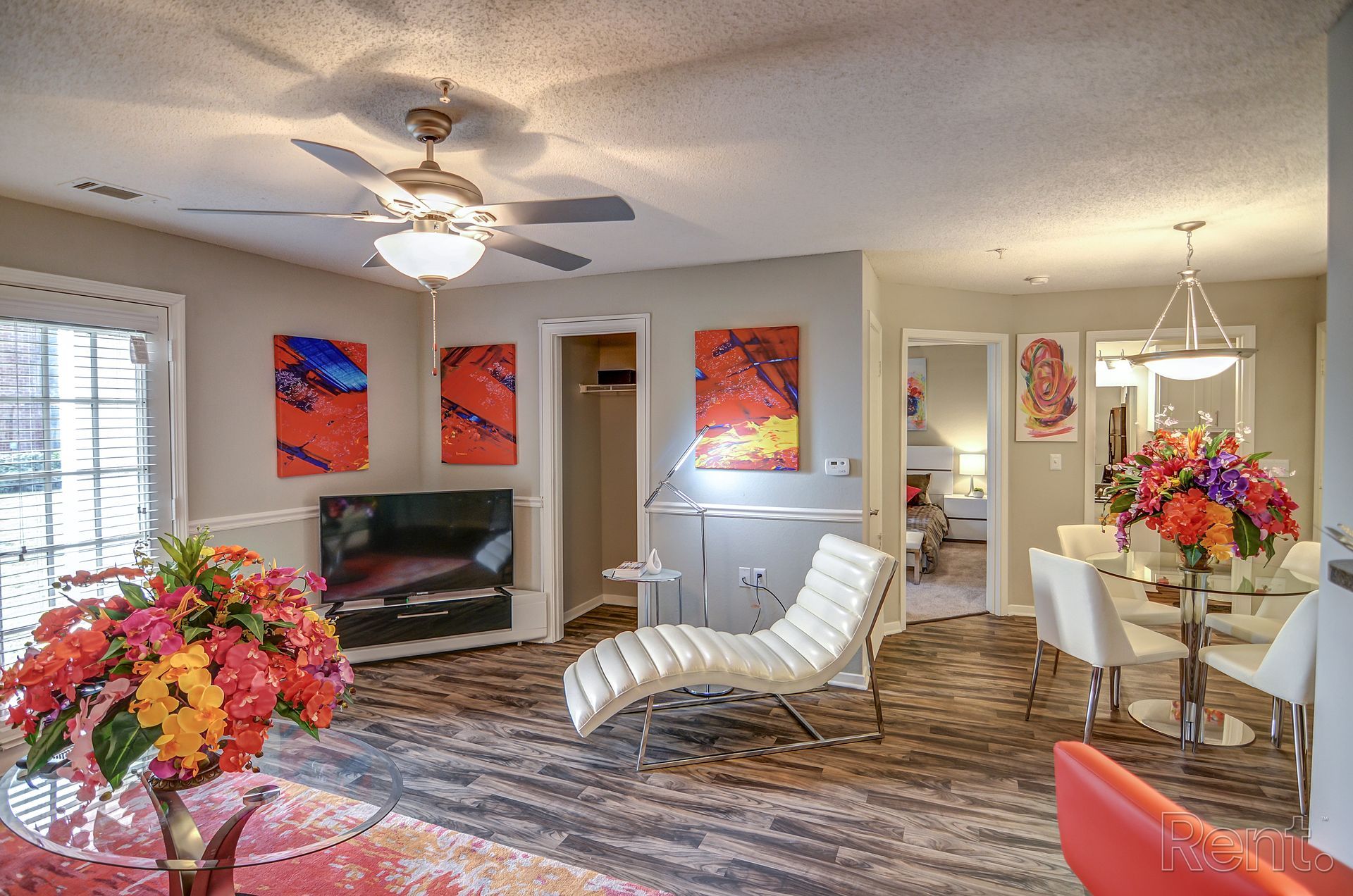 A living room with a ceiling fan , a chair , a table and a vase of flowers.
