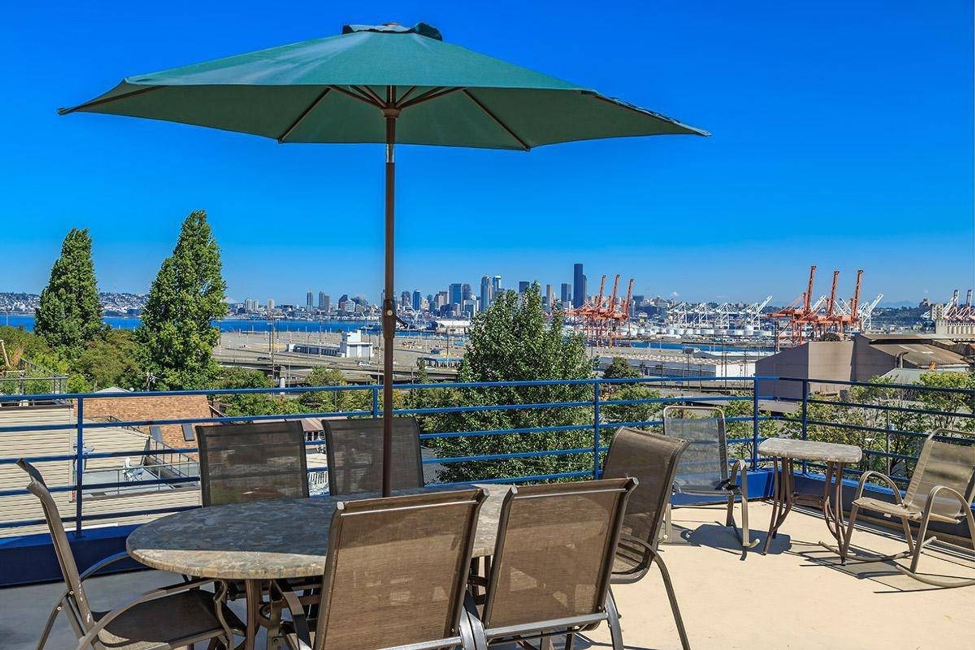 Rooftop patio with table, chairs, and large umbrella overlooking a harbor and city skyline