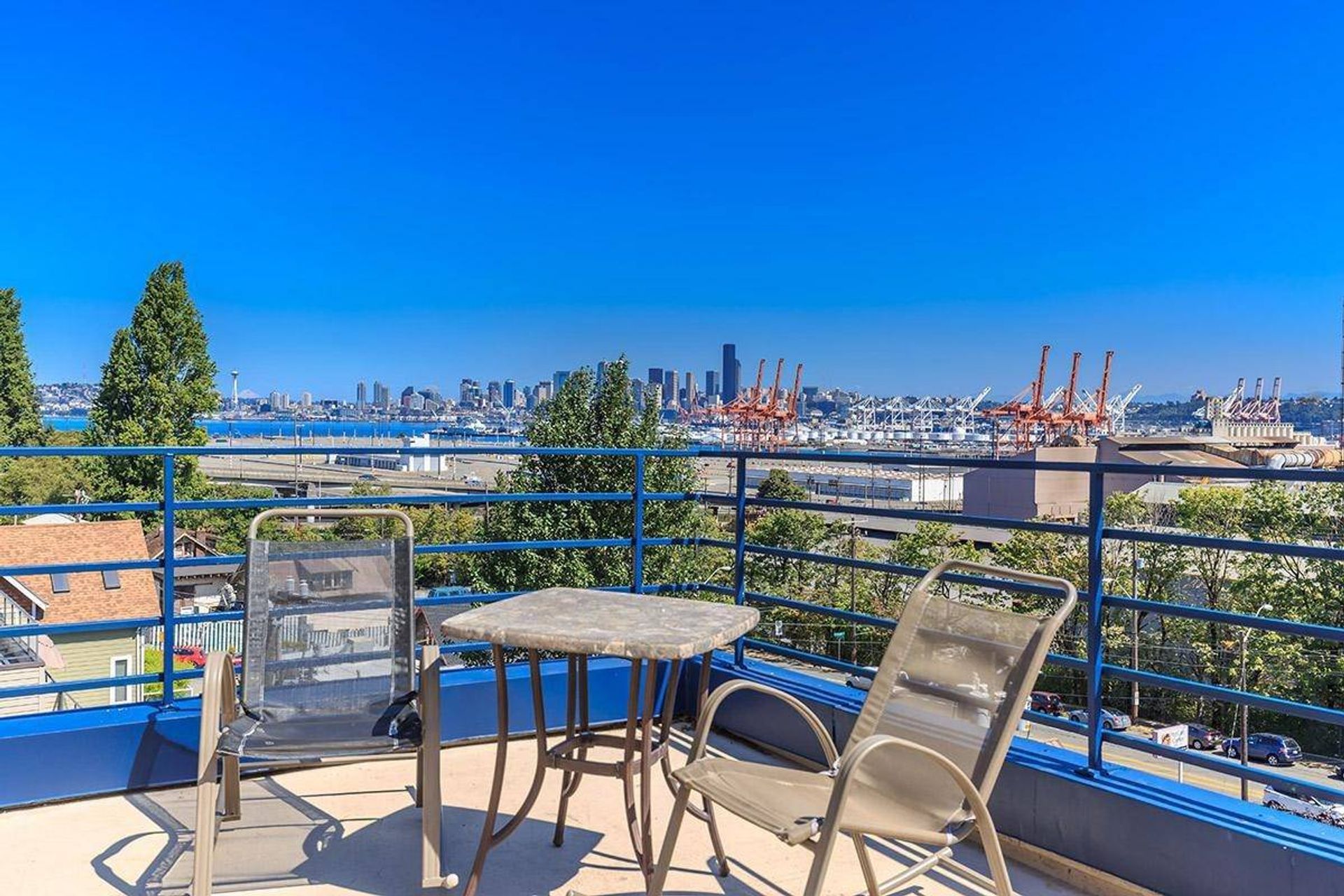 Balcony patio with table and chairs overlooking a harbor and city skyline under a clear blue sky