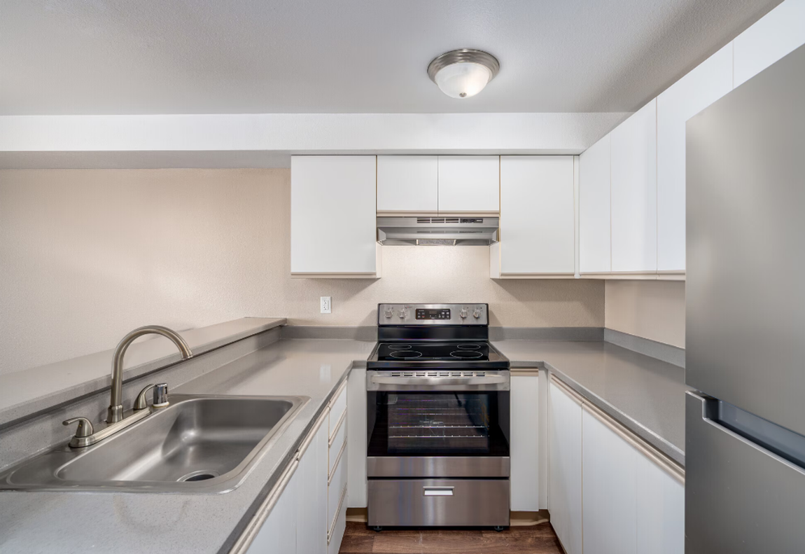 Bright modern galley kitchen with white cabinets, stainless appliances, and gray countertops