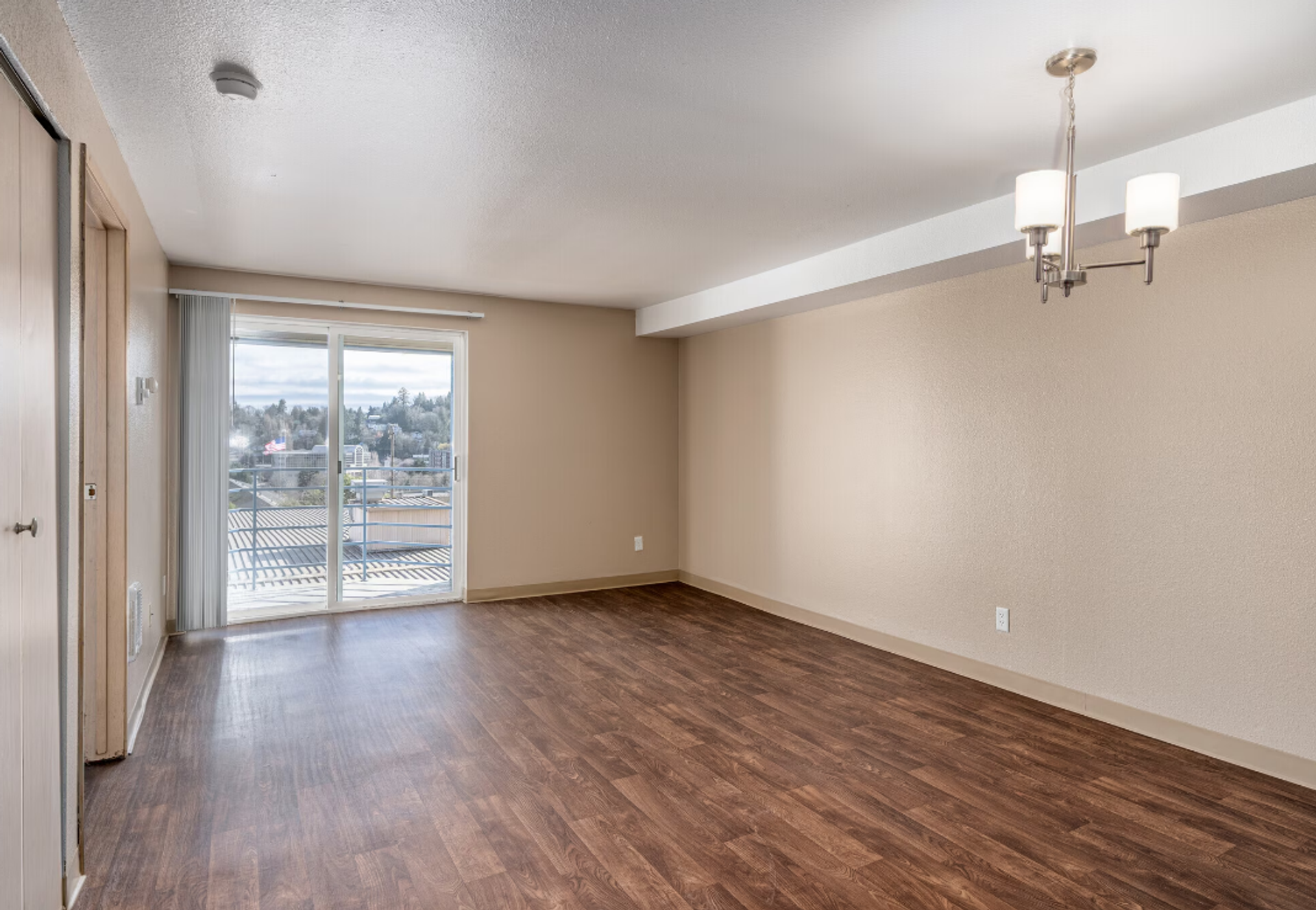 Empty beige living room with wood floors and sliding glass doors to a balcony.