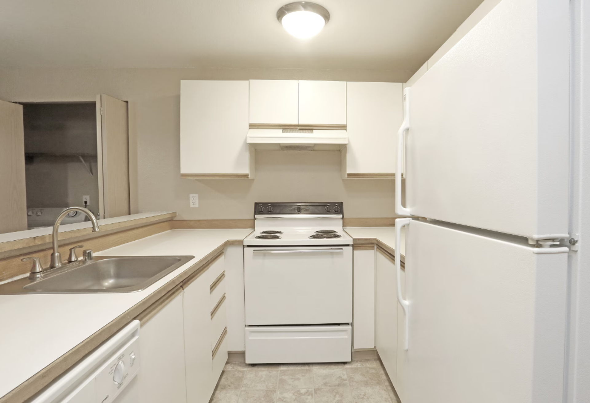 Small white kitchen with sink, stove, and refrigerator under bright ceiling light.