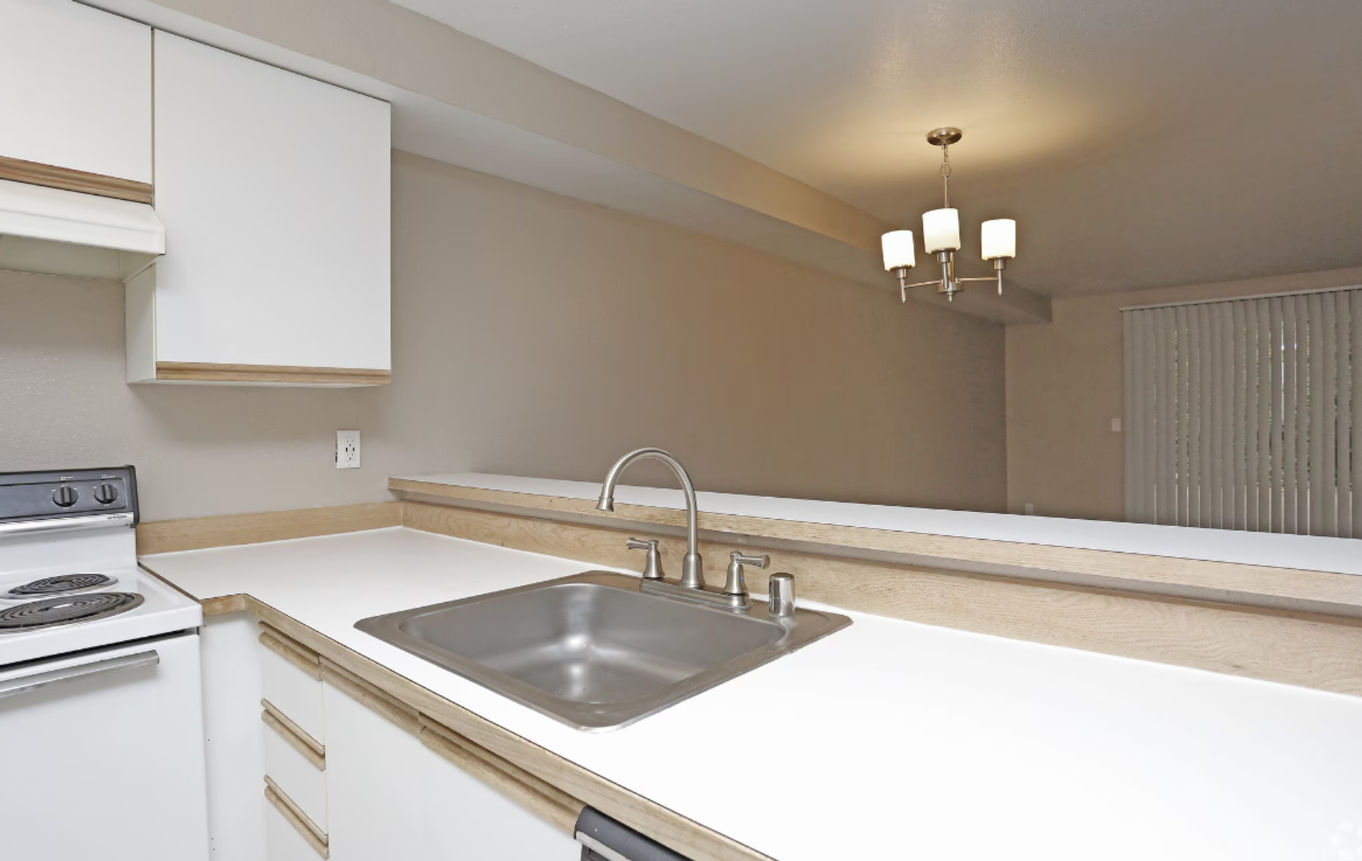 Bright kitchen with white cabinets, countertop, sink, stove, and a pass-through opening to a dining area