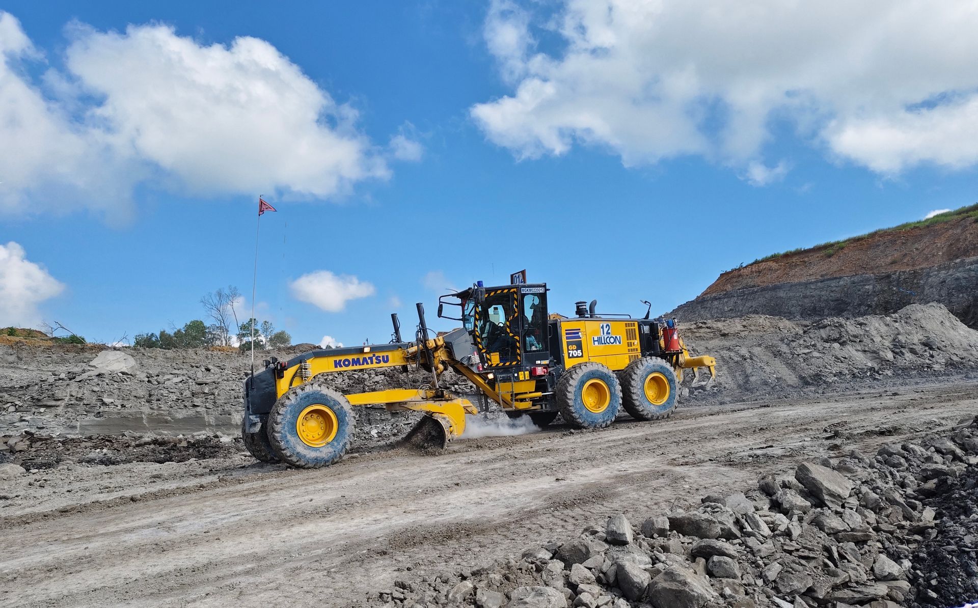 Yellow motor grader operating on a dirt road, under a blue sky.