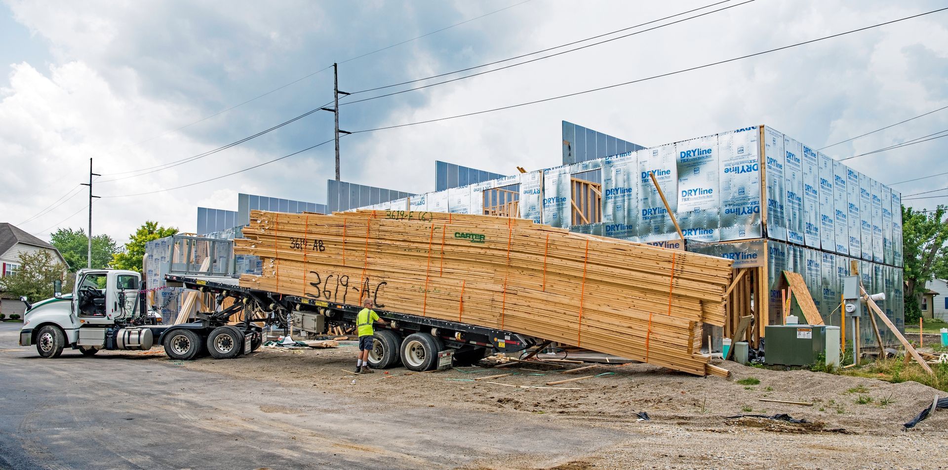 A semi-truck unloading lumber at a building construction site on a cloudy day.