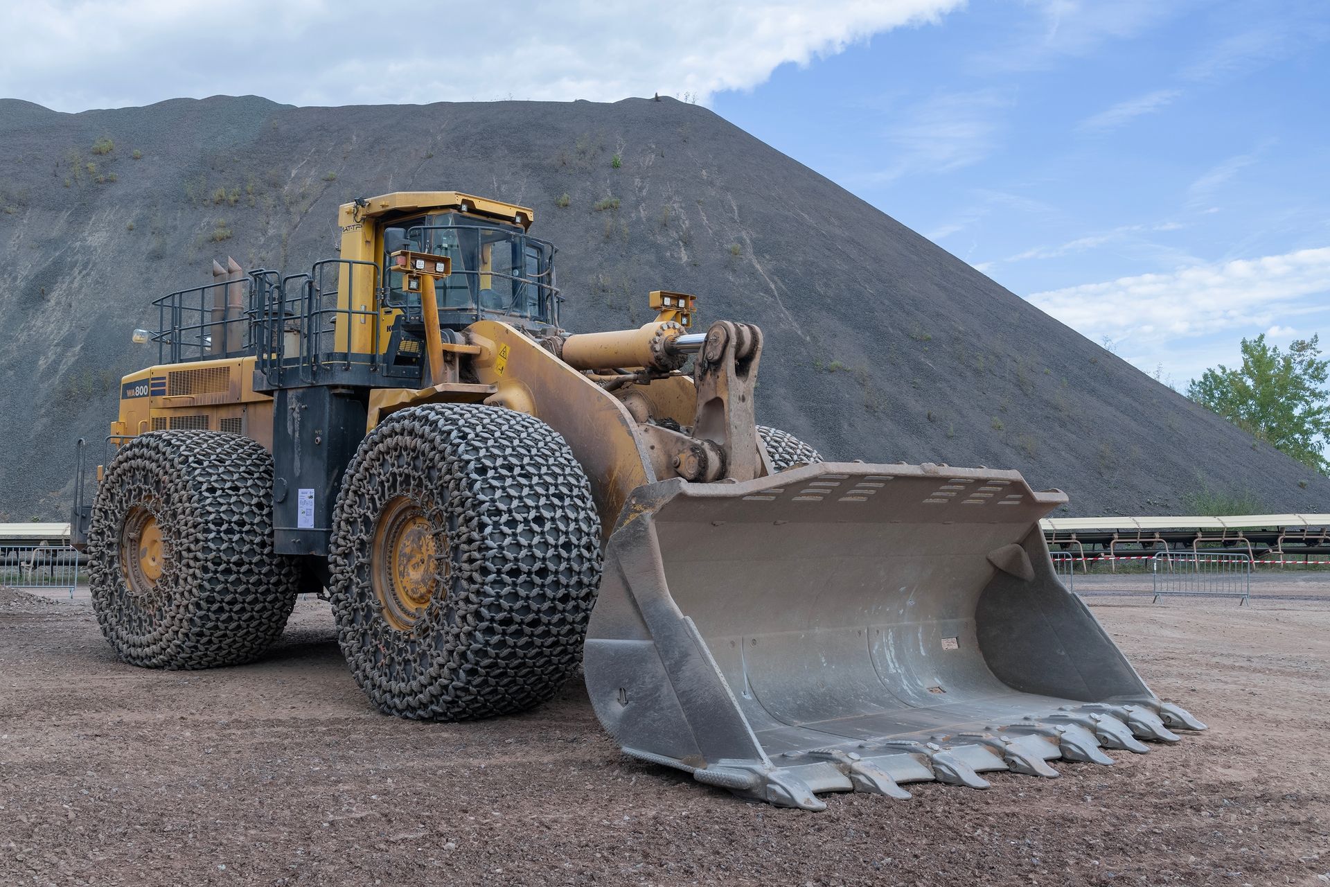 Yellow front-end loader with chain tires and large bucket in front of a pile of gravel.