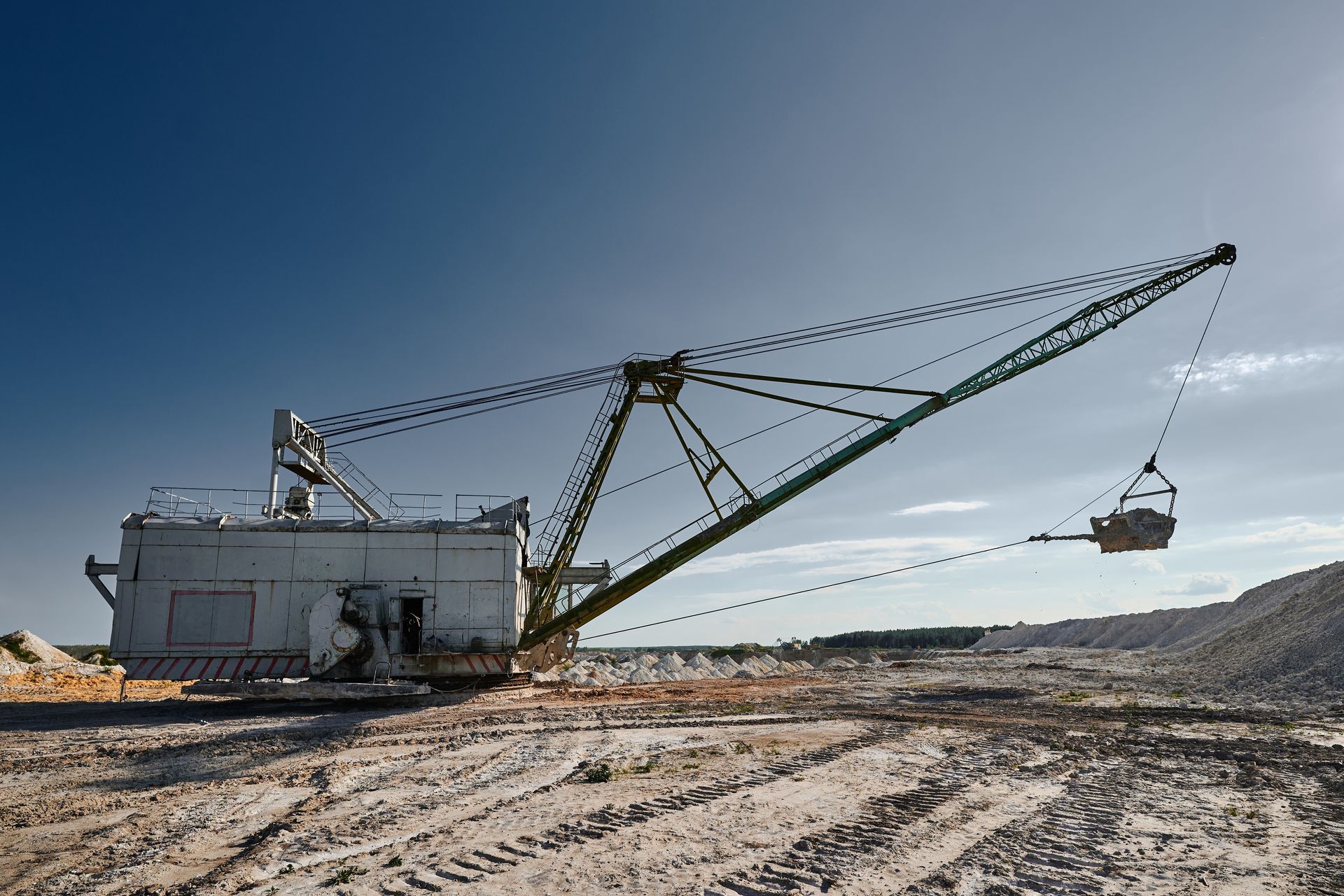 Large, white and green mining excavator on a dusty site under a blue sky.