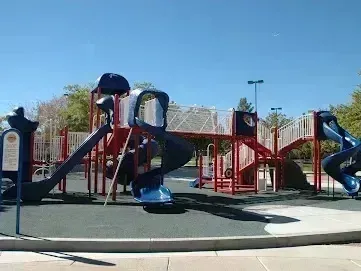 Henderson Artificial Turf - A playground featuring slides, a bridge, and various outdoor play equipment under a blue sky in a public park setting.