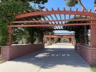 Henderson Artificial Turf- A covered outdoor walkway with red wooden beams and brick pillars, surrounded by greenery, under a clear blue sky.