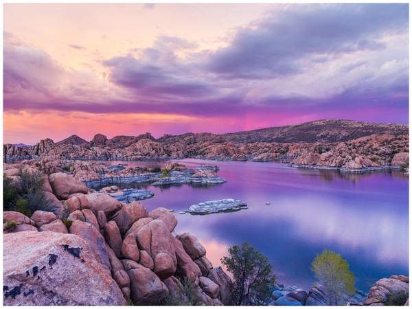 Lake surrounded by rocky formations under a sunset sky of purple and orange hues.