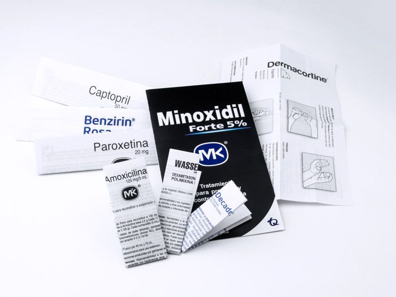 Envases y folletos de productos para el tratamiento de la caída del cabello con minoxidil sobre un fondo blanco.
