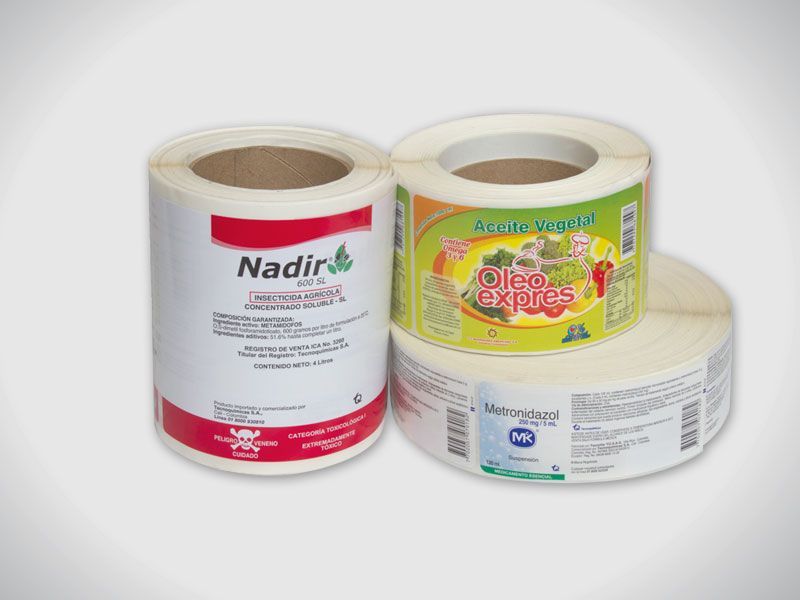 Tres rollos de cinta adhesiva para etiquetas en envases blancos, amarillos y color crema sobre un fondo claro.
