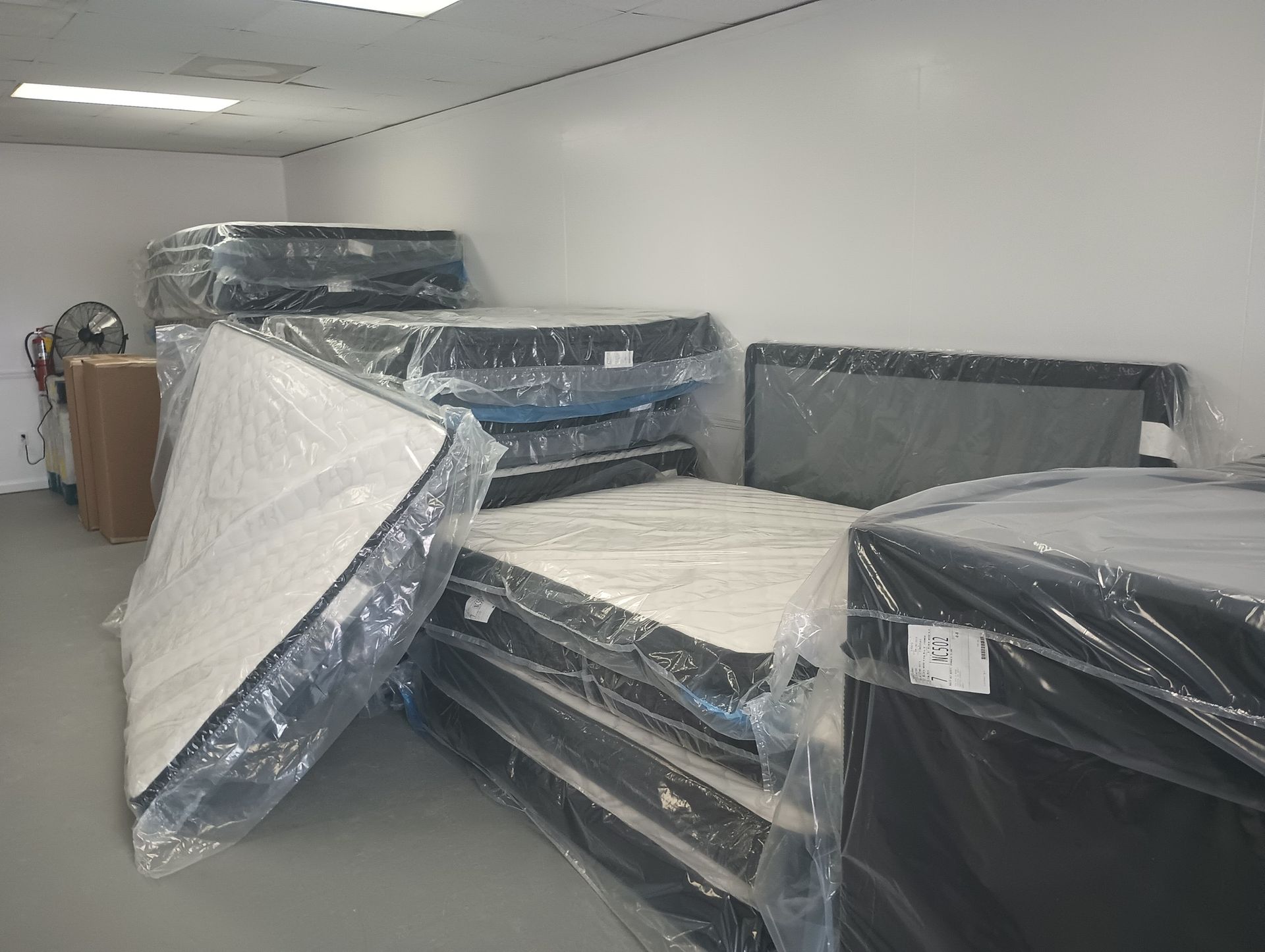 Mattresses wrapped in plastic stacked in a storage room.