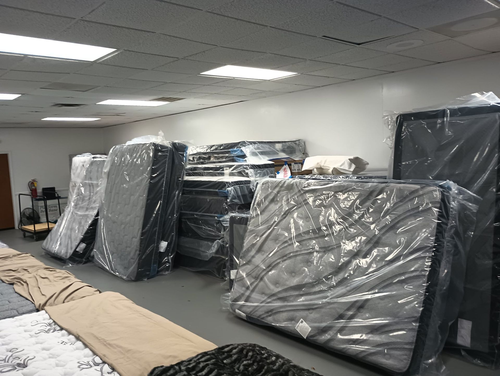 Mattresses in plastic wrap stacked in a well-lit showroom.