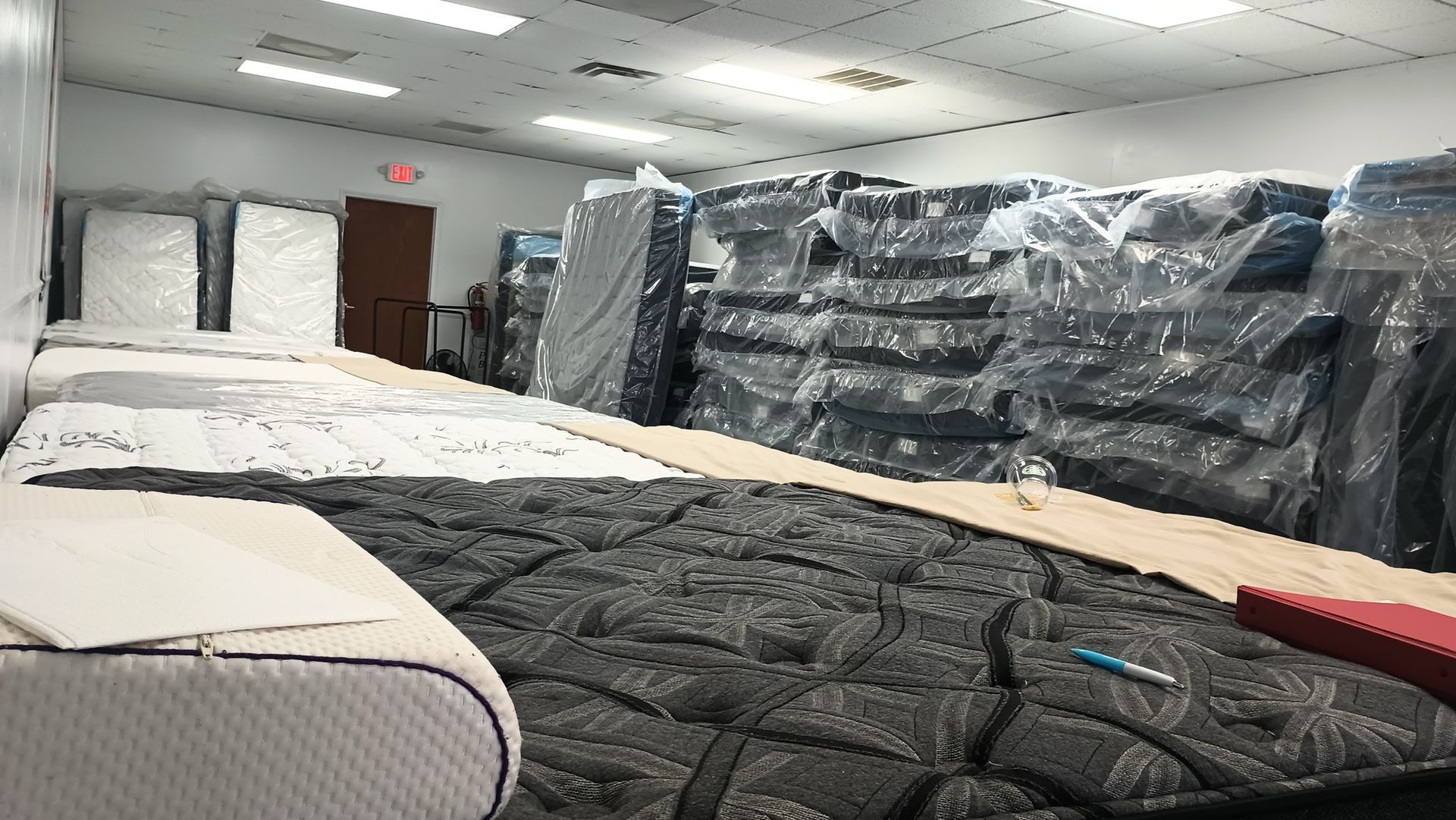 Mattress store interior with various mattresses on display and stacked, wrapped ones.