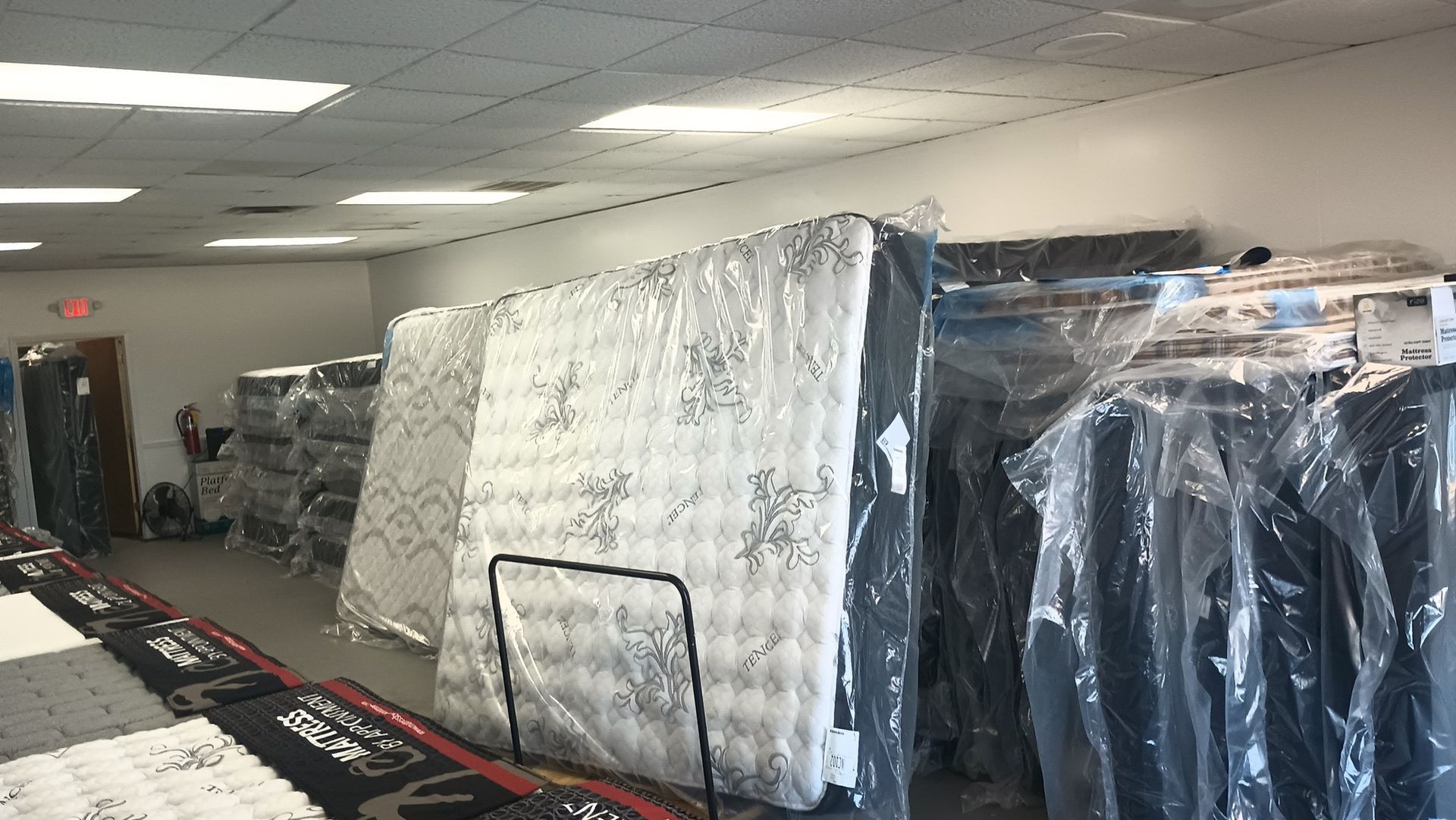 A warehouse-style retail space filled with rows of new mattresses wrapped in protective plastic.