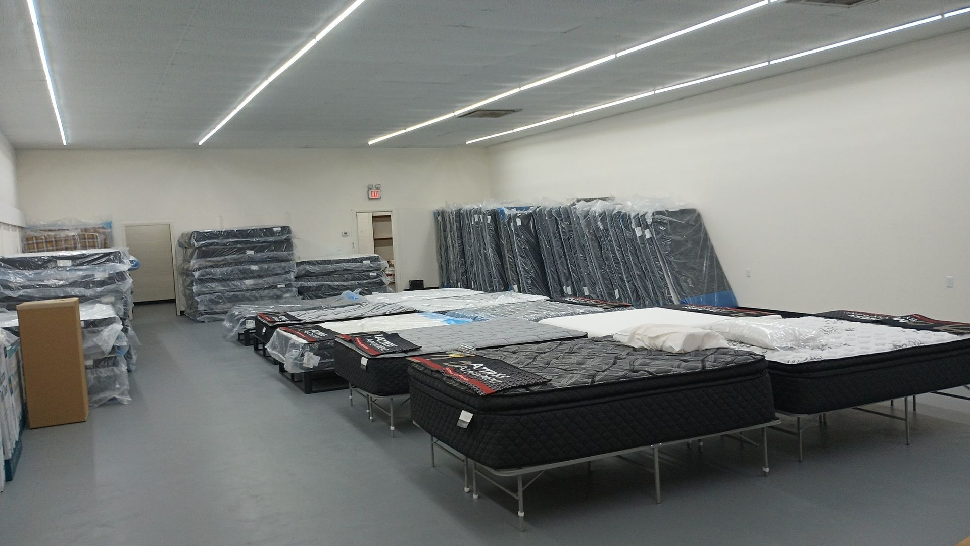 Warehouse filled with wrapped mattresses; fluorescent lights overhead.