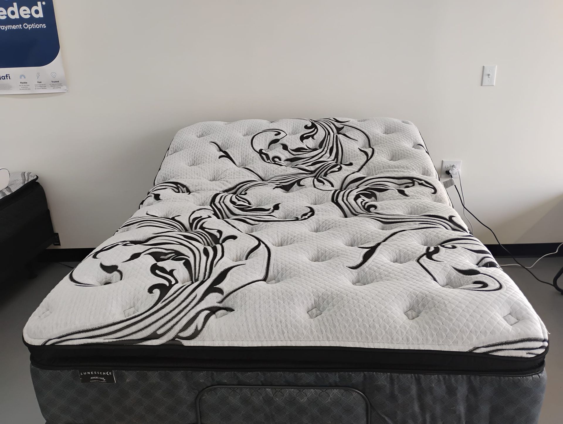 White and black patterned mattress on a dark grey base, in a room with a white wall.