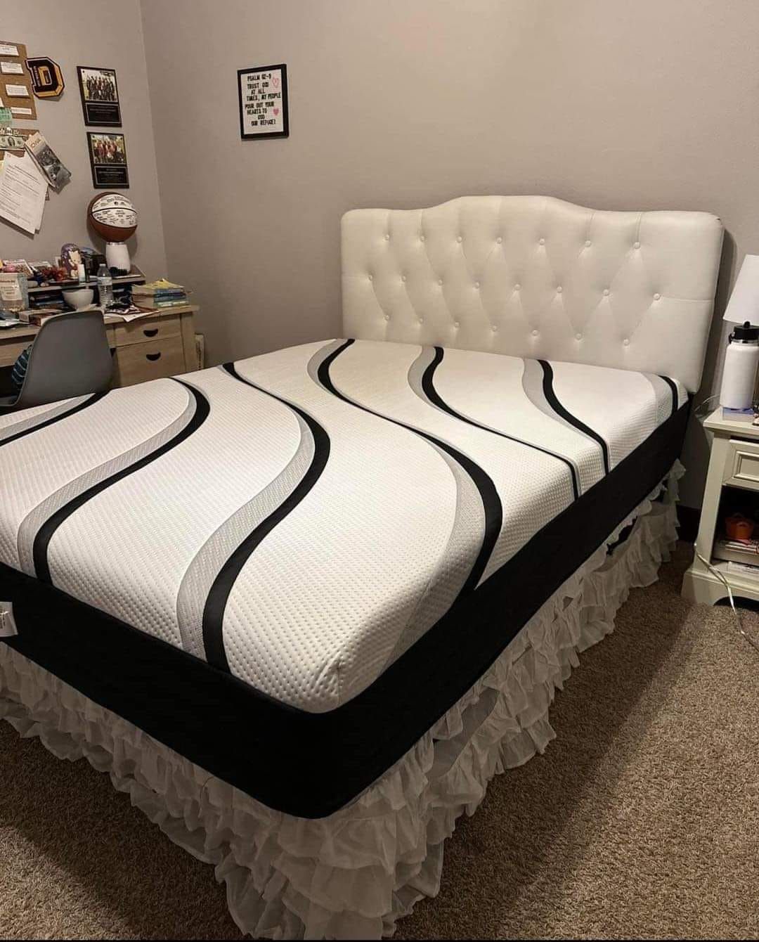 White upholstered bed with patterned mattress and ruffled bed skirt in a bedroom.