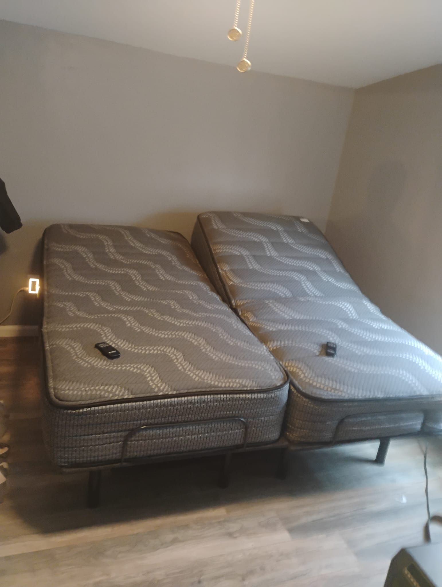 Two adjustable twin mattresses on a metal frame, in a bedroom with a light gray wall.