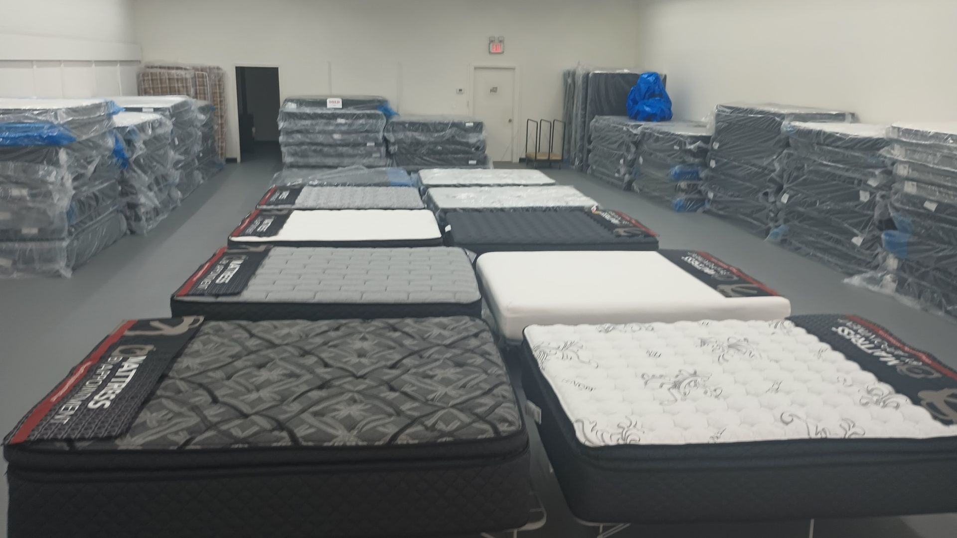 Warehouse with several mattresses on display and stacked, ready for sale.