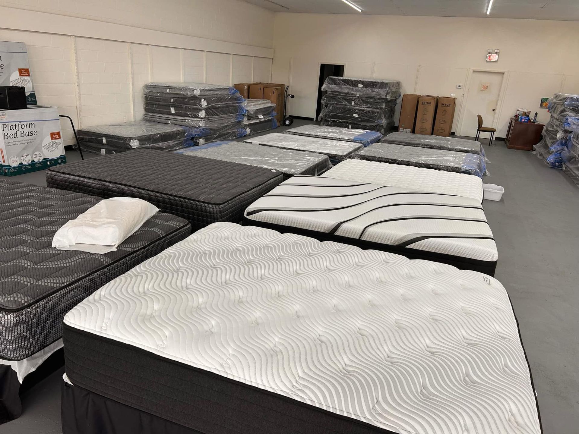Mattresses on display in a store, various styles and colors, some wrapped in plastic.