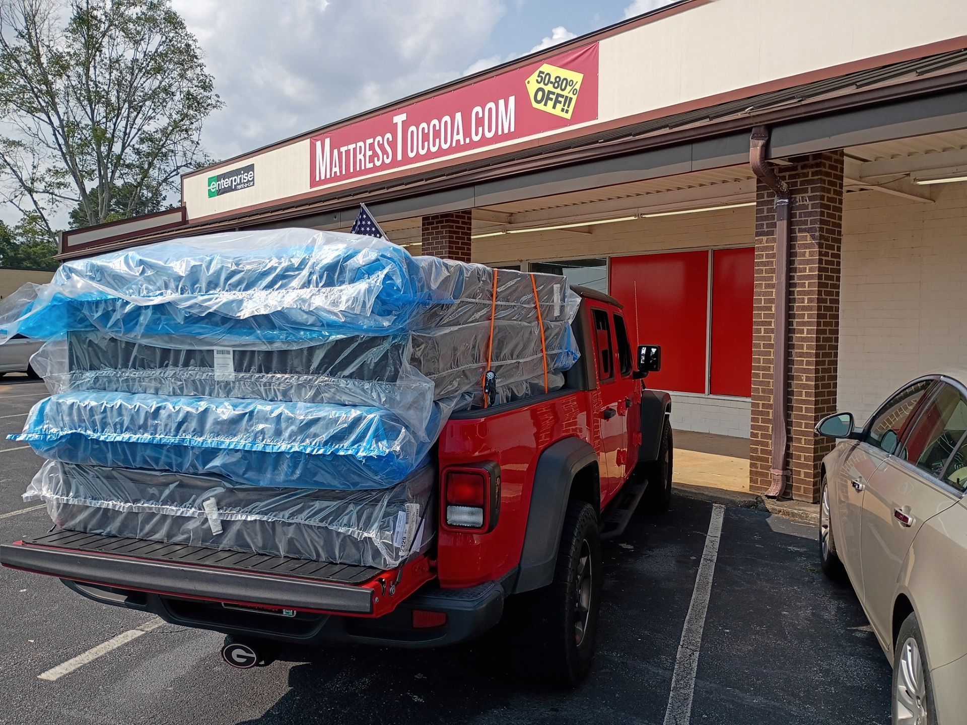 Red truck loaded with wrapped mattresses parked outside a mattress store.