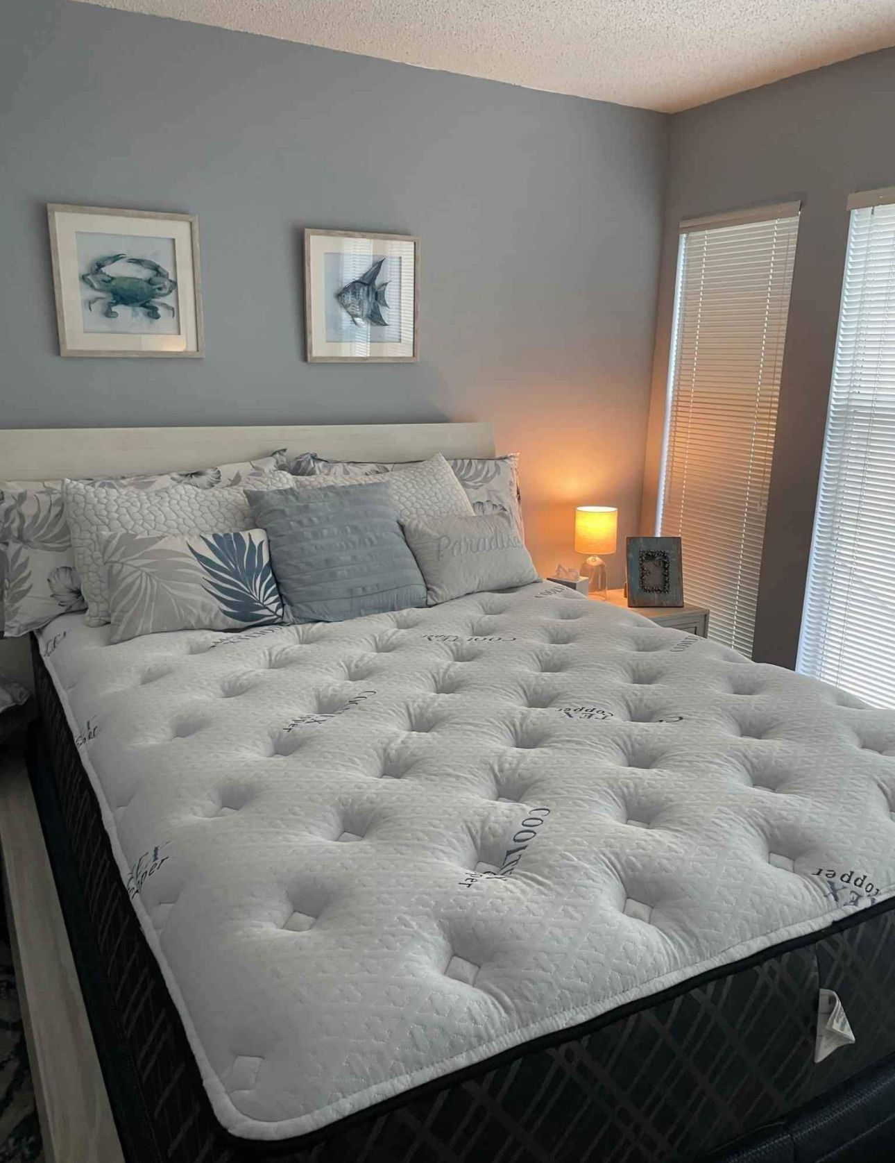 Bedroom with blue walls, a large tufted mattress, and ocean-themed artwork above the bed.