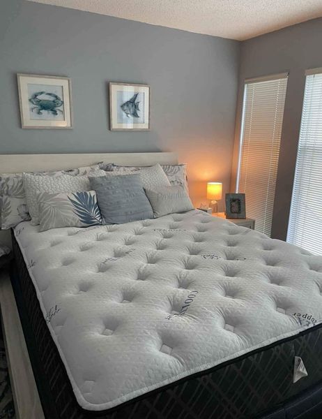 Bedroom with a bed, pillows, artwork, and a nightstand. Blue walls and natural light.
